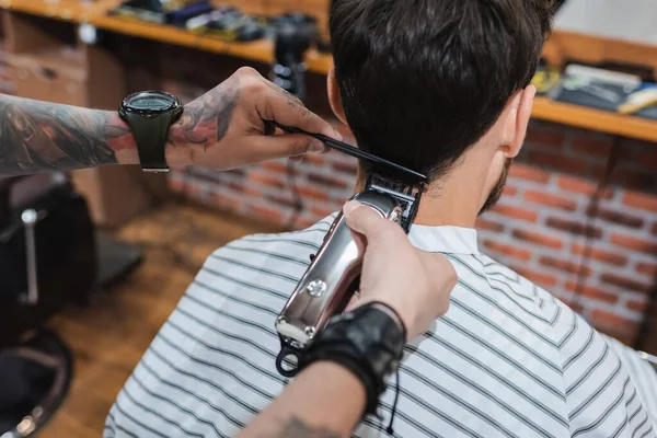 Brunette man near tattooed hairdresser trimming his neck with electric hair clipper — Stock Photo