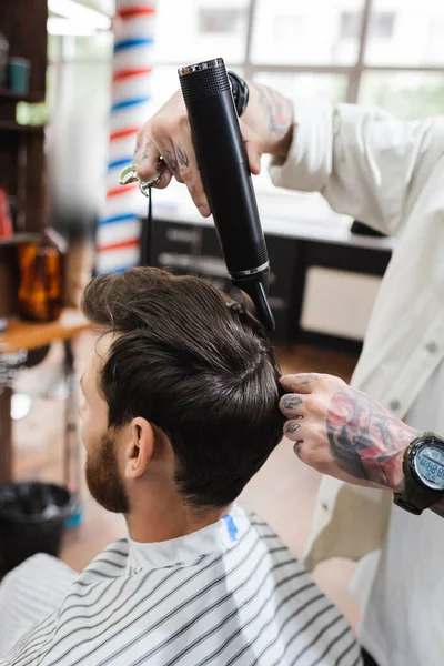 Peluquería tatuada en reloj de pulsera secado pelo del cliente en la barbería - foto de stock