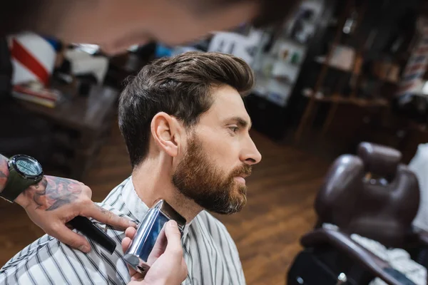 Morena barbudo hombre cerca barbero afeitándose el cuello con maquinilla de afeitar eléctrica - foto de stock