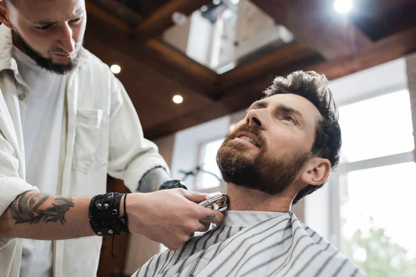 Bajo ángulo vista de peluquero afeitado cuello de hombre barbudo con afeitadora eléctrica - foto de stock