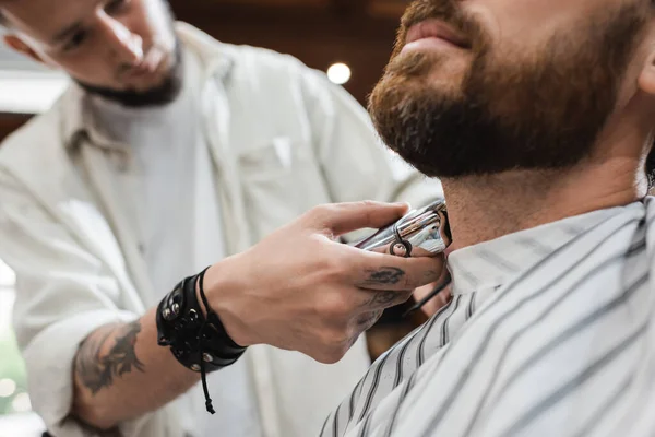 Vista parziale di barbiere sfocato collo da barba di uomo barbuto con rasoio elettrico — Foto stock