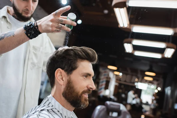 Татуированный парикмахер в кожаном браслете наносит текстурный порошок на волосы клиента — стоковое фото