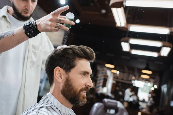 Tattooed barber in leather bracelet applying texture powder on hair of client — Stock Photo