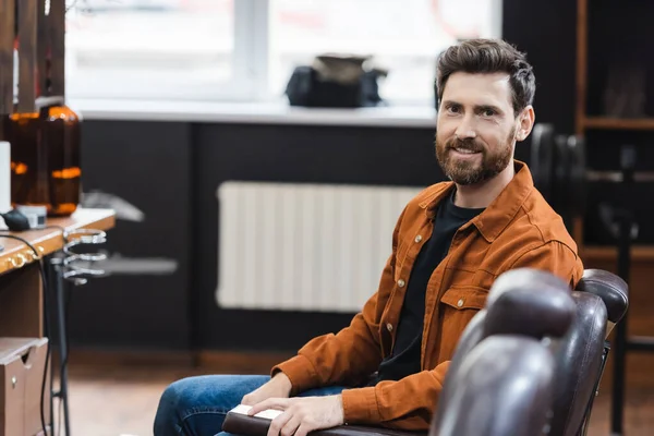 Bearded brunette man sitting in barbershop and looking at camera — Stock Photo