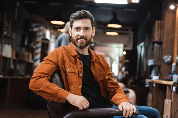 Morena barbudo homem sentado no salão de beleza e sorrindo para a câmera — Fotografia de Stock