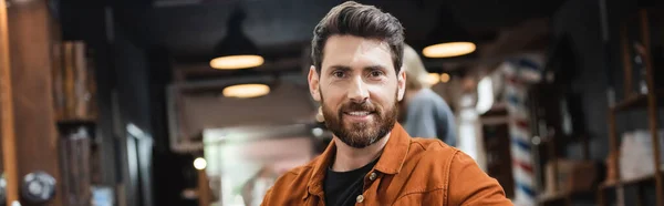 Hombre morena feliz con barba mirando a la cámara en el salón de belleza, pancarta - foto de stock