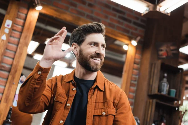 Sorrindo homem olhando para longe e acenando a mão na barbearia — Fotografia de Stock