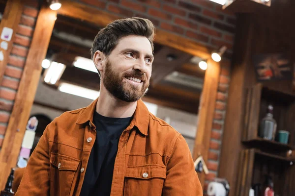 Hombre morena feliz con barba mirando hacia otro lado en el salón de belleza - foto de stock