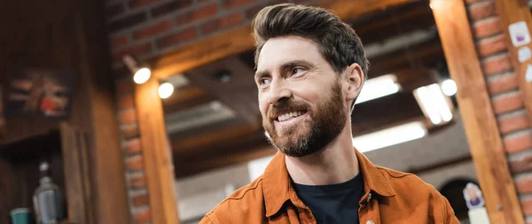 Bearded client of barbershop looking away and smiling on blurred background, banner — Stock Photo