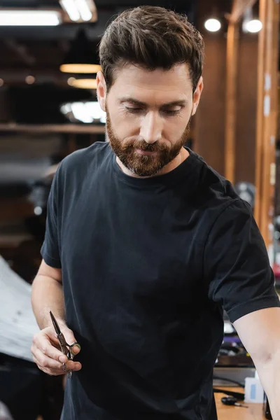 Бородата брюнетка перукар тримає ножиці в салоні краси — стокове фото