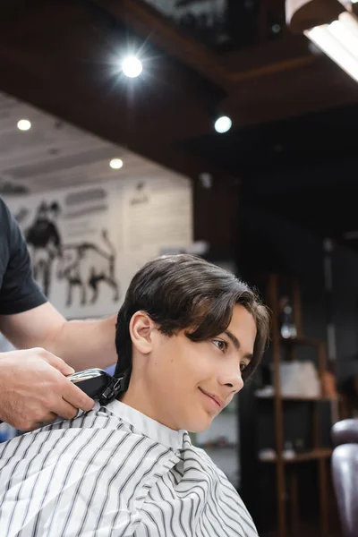 Coiffeur coupe cheveux de sourire adolescent gars dans le salon de coiffure — Photo de stock