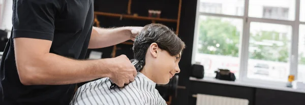 Vista lateral do cabeleireiro aparar o pescoço do cliente adolescente na barbearia, banner — Fotografia de Stock