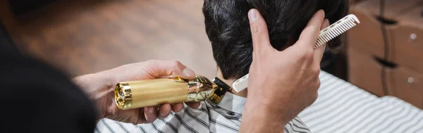 Cropped view of barber holding comb and trimming hair of teenage boy, banner — Stock Photo