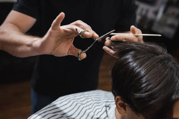 Hairdresser cutting hair of brunette teenager in barbershop — Stock Photo