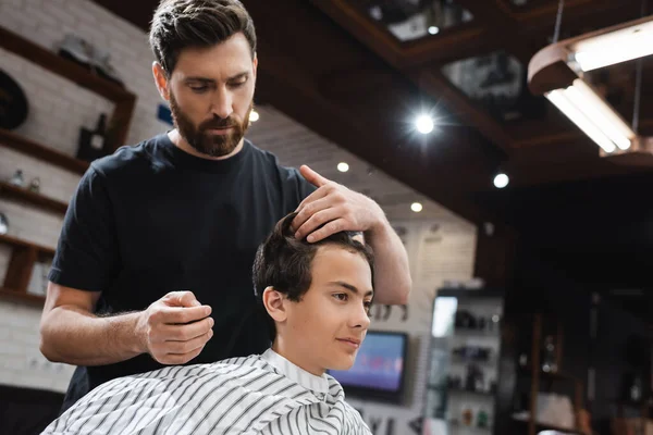 Peluquero barbudo tocando el pelo de chico morena en salón de belleza - foto de stock