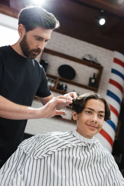 Barbeiro corte cabelo de morena adolescente sentado na capa de cabeleireiro — Fotografia de Stock