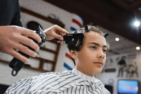 Adolescente con horquillas cerca de peluquero peinándose el pelo y sujetando el cortador de pelo - foto de stock