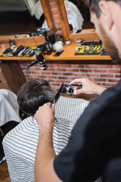 Coiffeur flou couper les cheveux de l'adolescent avec tondeuse dans le salon de beauté — Photo de stock