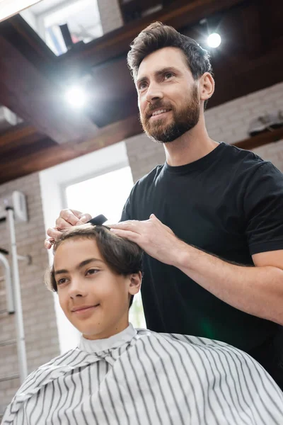 Усміхнений перукар розчісує волосся хлопчика-підлітка в салоні краси — стокове фото