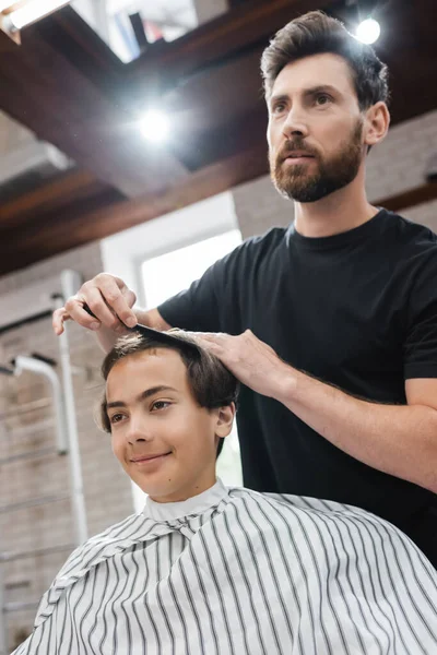 Cabeleireiro pentear o cabelo do cliente adolescente no salão de beleza — Fotografia de Stock