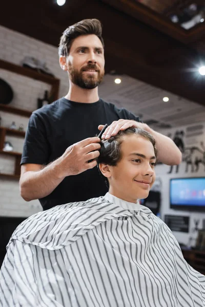 Alegre peluquero peinando pelo de adolescente en salón de belleza - foto de stock