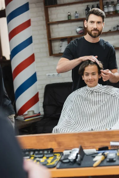 Accogliente parrucchiere pettinando i capelli del cliente adolescente in barbiere — Foto stock