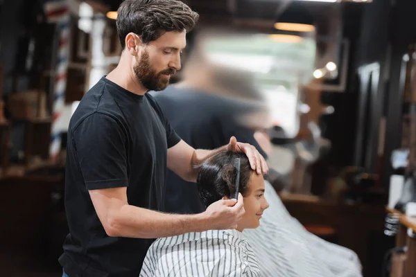 Barba parrucchiere pettinatura capelli di adolescente in mantello in salone di bellezza — Foto stock