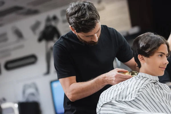 Cabeleireiro aparar o cabelo de adolescente com clipper no salão de beleza — Fotografia de Stock