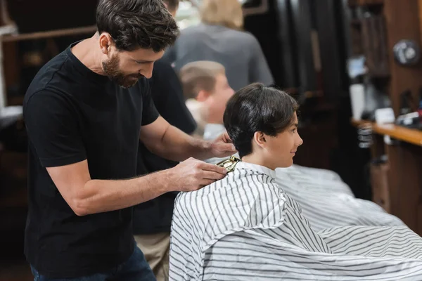 Coiffeur barbu couper les cheveux du garçon adolescent dans le salon de beauté — Photo de stock