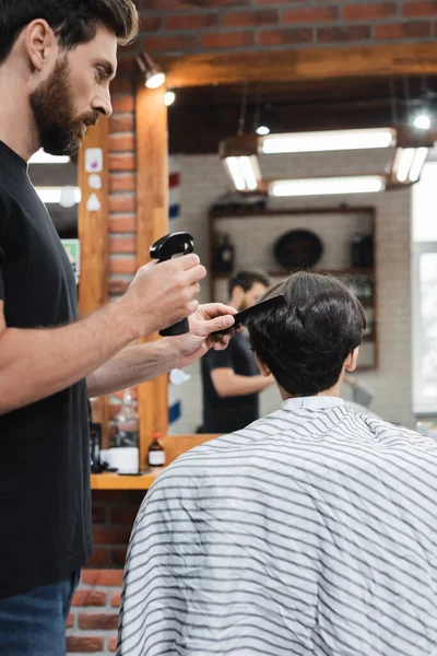 Hairdresser holding sprayer while combing hair of client in beauty salon — Stock Photo