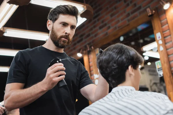 Coiffeur pulvérisation d'eau sur les cheveux du garçon adolescent flou dans le salon de beauté — Photo de stock