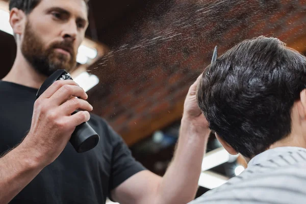 Low angle view of blurred hairdresser spraying water on hair of teen boy in beauty salon — Stock Photo