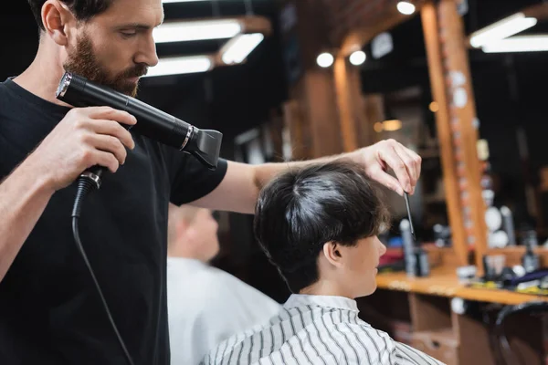 Peluquería secado cabello de cliente adolescente en salón de belleza - foto de stock