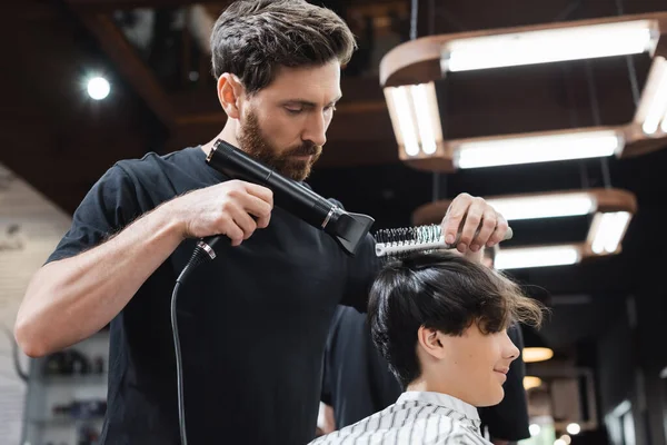 Barbiere asciugando capelli di ragazzo adolescente in mantello di parrucchiere in salone di bellezza — Foto stock