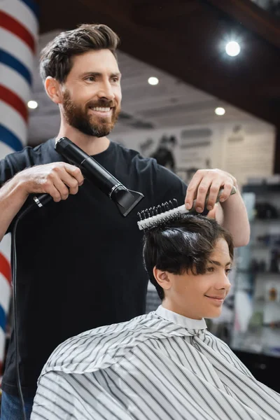 Cabelo de secagem barbeiro feliz de adolescente sorridente na capa de cabeleireiro no salão de beleza — Fotografia de Stock