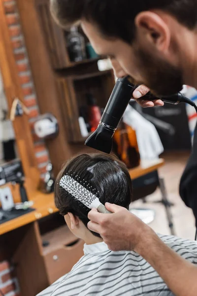 Blurred hairstylist combing and drying hair of teenage boy in beauty salon — Stock Photo