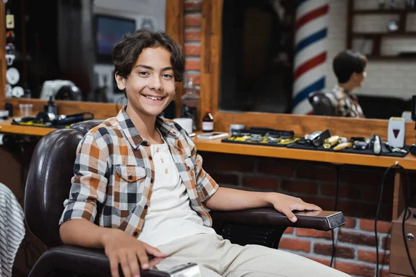 Sorrindo adolescente menino olhando para a câmera na barbearia — Fotografia de Stock