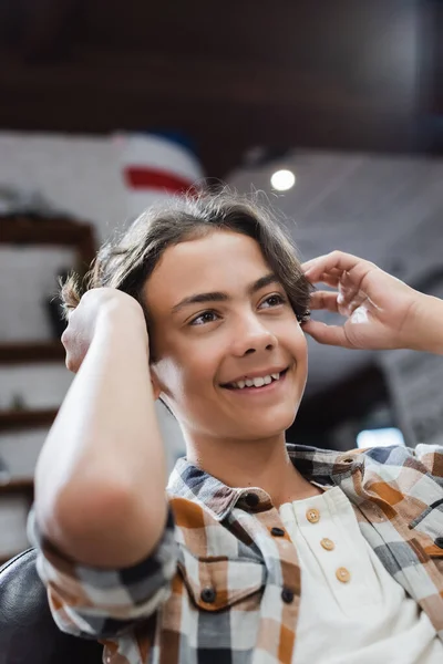 Joyeux adolescent garçon ajuster les cheveux dans le salon de beauté — Photo de stock