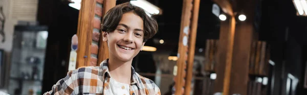 Adolescente sonriendo a la cámara cerca del espejo en la barbería, pancarta - foto de stock