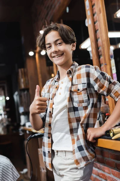 Teenage ragazzo mostrando come gesto a macchina fotografica in sfocato barbiere — Foto stock