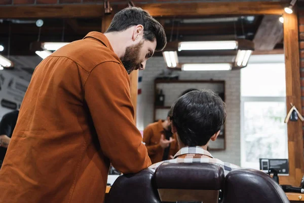 Barbe barbier parler à adolescent client dans fauteuil dans salon de coiffure — Photo de stock