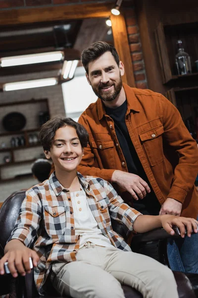 Peluquero y adolescente sonriendo a la cámara en la barbería - foto de stock