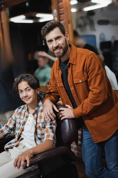 Positive teenager and hairstylist looking at camera in beauty salon — Stock Photo