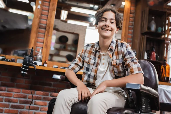 Positive teenage boy in casual clothes looking at camera in barbershop — Stock Photo