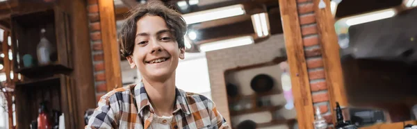 Rapaz adolescente feliz olhando para a câmera na barbearia borrada, banner — Fotografia de Stock
