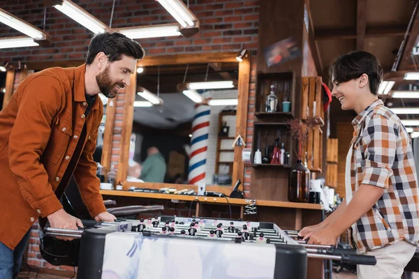 Vista lateral de sonriente padre e hijo jugando futbolín en barbería — Stock Photo