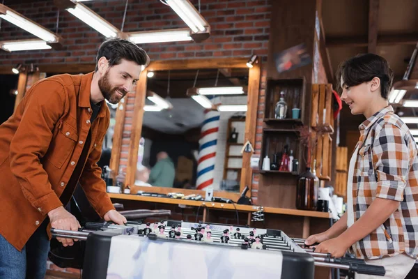 Smiling dad and teenage son playing table football in barbershop — Stock Photo