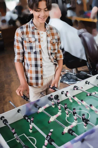 Усміхнений хлопчик-підліток грає у настільний футбол у перукарні — стокове фото