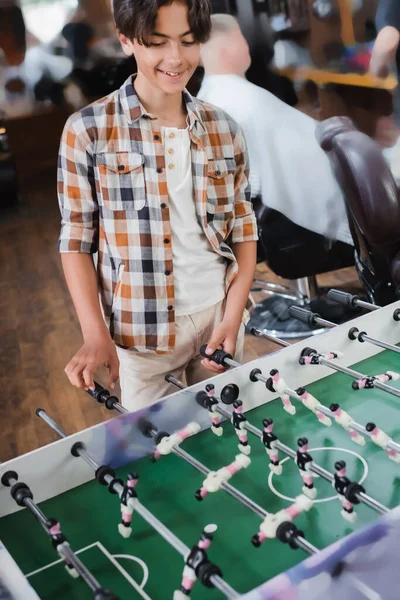 Sonriente adolescente jugando futbolín en barbería - foto de stock