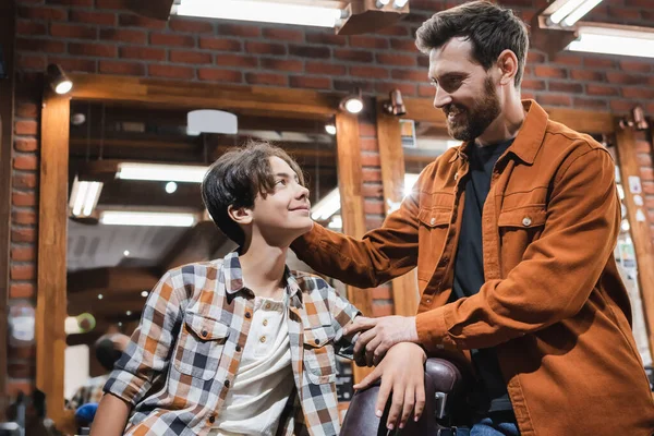 Smiling hairdresser looking at teenage boy in barbershop — Stock Photo